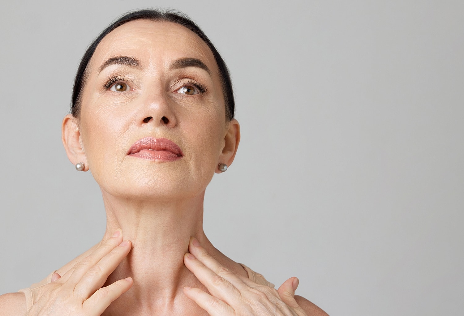 Woman gently touching her neck, looking upwards.