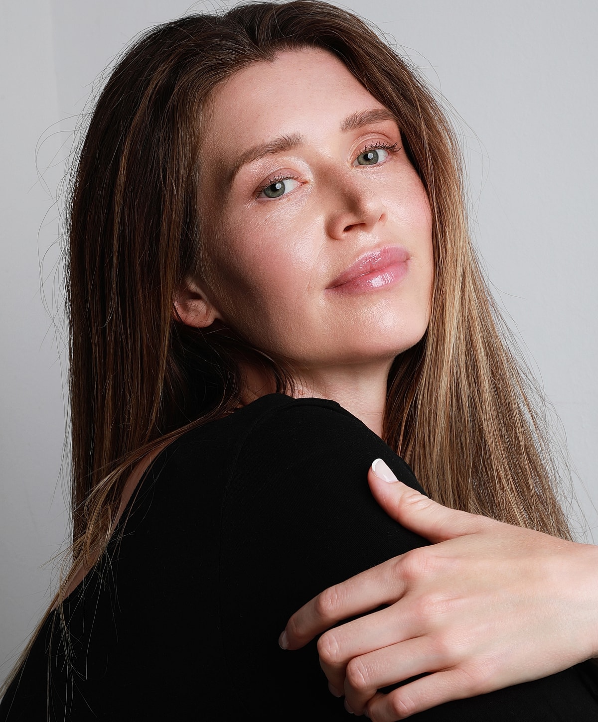Woman with long hair posing thoughtfully against wall.